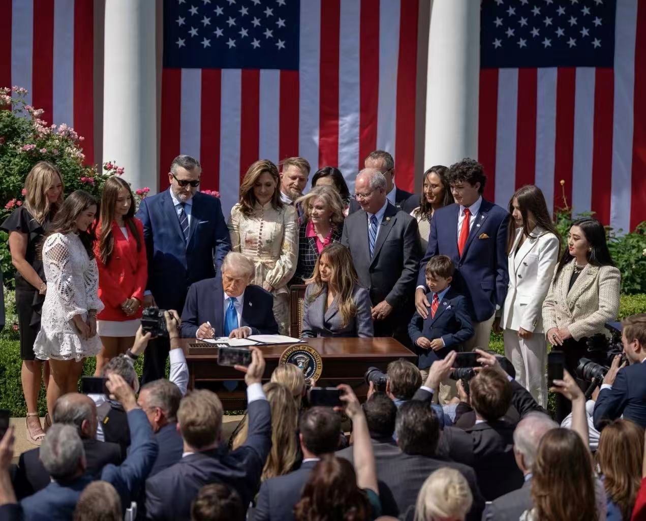 White House bill-signing ceremony in the Rose Garden with attendees and U.S. flags.